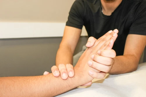 Clinician stabilizing a patient's forearm and wrist during a medical examination or treatment on a treatment table.