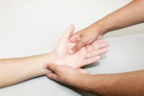 Two hands hold and steady a forearm and wrist against a light background, as in a medical check.