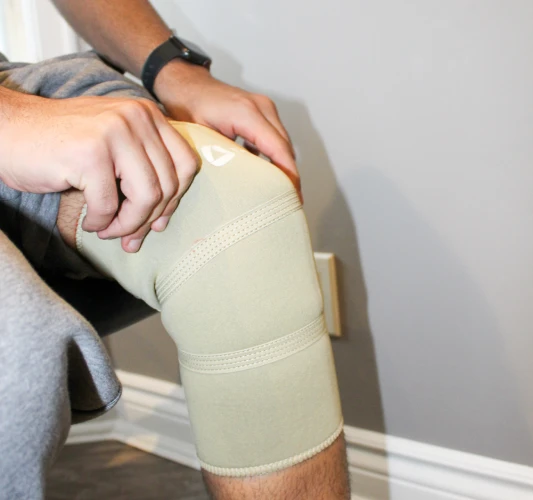 Close-up of hands adjusting a beige knee brace on a seated person’s leg.
