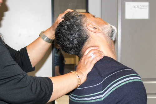 Person giving a neck massage to a man who is seated, his head tilted back for the treatment.