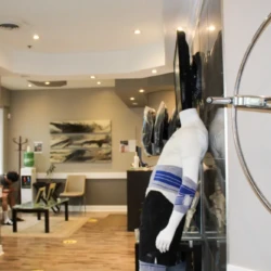 Showroom interior with a mannequin on display wearing a white and blue striped outfit, seating area in the back, and abstract art on the wall.Chairs and a glass table seen in a contemporary lobby setting.