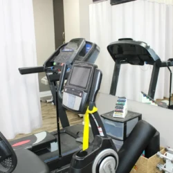Treadmill and stationary bike in a small gym with a mirror and free weights nearby.