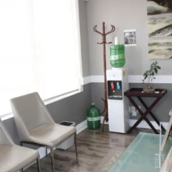 Waiting area with four beige chairs around a glass coffee table, a water cooler, and wall art in a modern office space.
