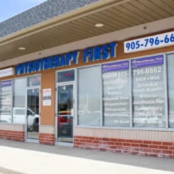 Exterior view of Physiotherapy First clinic in a strip mall; blue sign reads 'PHYSIOTHERAPY FIRST' with phone number 905-796-6662 and large front windows showing services inside.